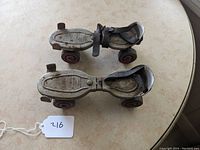 Side view of the pair of vintage roller skates showing metal baseplates, black rubber straps, and rusty wheels.