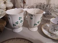 Two white ceramic Irish coffee cups decorated with green shamrocks, shown together on a table