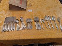 Full set of utensils laid out on a yellow patterned tablecloth including knives, spoons, forks, and serving pieces.