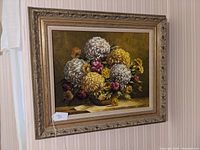 Framed still life flower oil painting hanging on a wall, showing full front view with bouquet of yellow and white chrysanthemums and pink flowers.