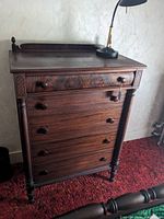 Full frontal shot of the tall colonial style mahogany dresser with five drawers and a lamp on top.