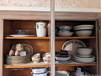 Two wooden shelves filled with assorted dishware and kitchenware including Franciscan Desert Rose pieces and other items.