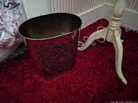 Side view of vintage brass waste paper basket showing ornate decorative pattern and oval shape.