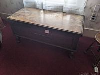 Front view of cedar chest showing carved front panel, worn top and dark wood finish.