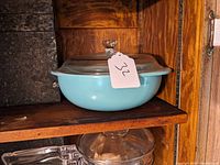 Side view of the turquoise blue Pyrex casserole dish with glass lid on a wooden shelf.