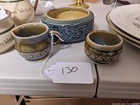 Front view of two small glazed pottery items (creamer and sugar bowl) along with larger blue-gray pottery bowl with raised Celtic knotwork design