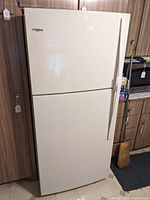 Front view of white Whirlpool top freezer refrigerator freezer showing upper freezer door and lower refrigerator door with vertical handles.