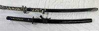 Both swords shown side by side lying flat, black sheaths and cord wrapped handles visible.