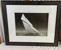 Framed black and white print featuring a sailboat in the ocean with full sails, capturing details of the boat and water reflections.