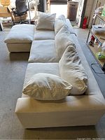 Photo of L-shaped white/off-white fabric sofa with cushions; shows overall sofa shape and condition with minor staining and dirt spots.
