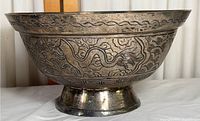 Side angle showing dragon and wave etched design on cast brass bowl with raised base