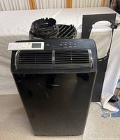 Front view of the black Midea mobile air conditioner with remote on top and vent tube behind. Shows scratches on front.