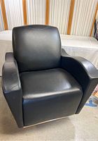 Front view of the modern black vinyl chair showing cushioned backrest, seat, and wide armrests