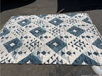 Full view of the blue and white plush Moroccan-style geometric shag rug displayed on asphalt surface, showing pattern and size.