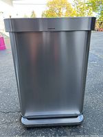 Front view of rectangular stainless steel trash can with step pedal, showing brushed metal finish and minor surface wear.