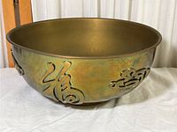 Full view of vintage round brass bowl with raised Chinese calligraphy characters on the side, showing patina and color variation.