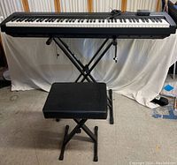 Full view of digital piano on stand with bench, pedal and power adapter