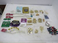 Overhead image showing assorted beads and jewelry findings laid out on a white surface including several plastic packages and small plastic bags.