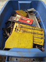 Box filled with mixed drill bits including some in yellow cases and blister packs, showing surface rust on several bits.