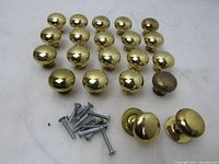 21 brass furniture knobs with screws, mostly round and similar size, arranged on white background.