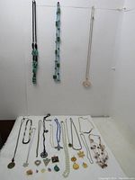 Photo showing variety of necklaces and pendants laid out on a flat surface. Necklaces include chains and beaded designs. Pendants include various styles and shapes.