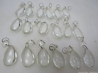 Lot of 18 clear glass tea drop prisms arranged on white surface, showing all individual items and metal loops for hanging.