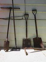Full view of all five hand tools lined up against a beige wall, showing handles and metal heads.