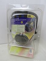 Front view of the 3M full face spray paint respirator in original clear plastic packaging showing label details and mask shape.