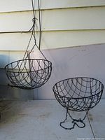 Two large metal hanging wire baskets shown side by side, one hanging from a hook, the other resting on a surface to show shape and size.