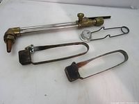 Oxy acetylene cutting torch with three metal strikers placed on white surface. Torch shows brass construction with copper tip. Strikers vary in shape and handle style, some oxidation visible.
