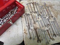 Photo showing 38 assorted combination wrenches laid out beside red tool box containing sockets.