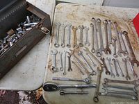 Photo showing 39 various combination wrenches arranged on a surface next to a metal toolbox containing multiple sockets and some ratchets