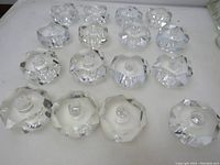 Top-down view of 16 faceted polished glass lamp spacers showing their clear multi-faceted shape and threaded central holes.