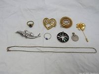 Full view showing all jewelry included in the lot laid out on white surface: two rings, silver necklace, Corocraft brooch, abalone inlay Mexican pendant, coin pendant, Cerrito flower brooch, and silver elongated brooch.