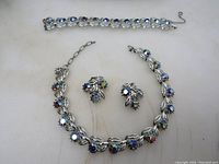 Full view of vintage blue sparkly glass necklace, bracelet, and clip-on earrings set on white background showing necklace incomplete with missing clasp and bracelet and earrings in good condition.