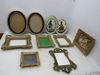Lot of 8 vintage plastic picture frames and 2 oval cross stitched cloth items displayed in a group. The frames vary in size, shape, and style, some with glass and some without. One frame contains a damaged mirror.