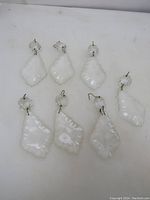 Seven vintage clear crystal chandelier prisms arranged on a white surface, showing front view with metal hooks visible.