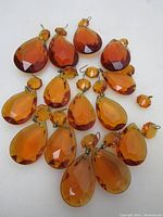 16 vintage amber tear drop prisms arranged in two groups; larger and smaller sizes with metal hooks, faceted surfaces catching light