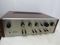 Front view showing the amplifier's control panel with power knob, volume, bass, treble, balance knobs and input selectors. Notable damage on power knob and one missing knob.