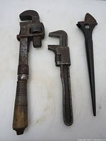 Front view of three wrenches; monkey wrench with wooden handle, pipe wrench, and adjustable wrench on white background.