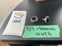 Two silver rings on black surface next to label indicating 925 & Sterling and 10.64 grams.