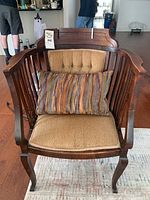 Front view of wooden accent chair with tan cushioned seat and backrest, and striped decorative pillow