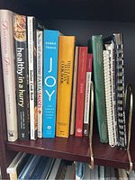 Photo showing a variety of assorted cooking books on a shelf, including titles such as Inspirational Jewels, Healthy in a Hurry, Italian Cookbook, Pasta Sauces, Joy by Debbie Travis, The Cake Cookbook, and The Dash Diet Cookbook.