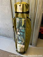 Packed green camp tent in cylindrical carrying bag with clear window showing tent features and brand.