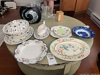Wide view of assortment of china pieces on a green round table, including plates, bowls, and a gravy boat.