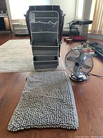 Photo of grey hanging organizer with clear pockets, grey bath mat with thick loops, and silver metal Bionaire desk fan on wooden floor
