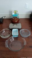 Photo of all items on a wooden surface including glass casseroles, blue metal baking dish, cookie jar, and glass storage containers.