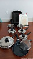 Full view of kitchenware including 2 graniteware roasting pans, 6 saucepans with lids, 1 frypan, sieve, cutting boards, and coaster arranged on floor.