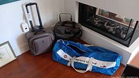 Photo showing all items in the lot: the Travelpro suitcase, Atlantic carry-on bag, Arctic Offshore duffel bag, and hand cart placed on wooden floor by a fireplace.