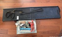 Full view of black pet ramp, two brown leather collars or leashes on ramp surface, small pet bed with five different plush toys inside it.